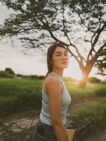Asian woman in casual sleeveless clothing strolls through a grassy countryside path under the golden...