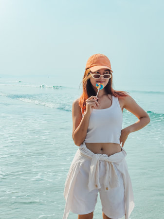 Young asian woman with colorful lollipop and orange hat enjoy the beach in Thailand.の写真素材
