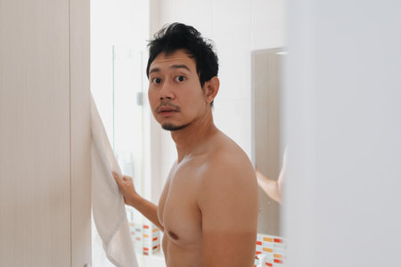 Shirtless Thai male with wet hair exiting bathroom holding towel in home settingの写真素材