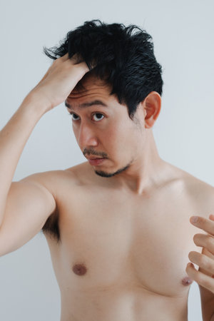 Shirtless Thai male fixing hairstyle while looking at reflection at home