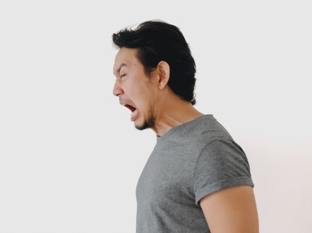 Asian man shows intense emotion, embodying anger and frustration in a side profile view reacting to a situationの写真素材
