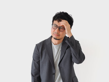 Man in a suit is looking down and shaking his head. He is wearing glasses and he is in a state of confusion or frustrationの写真素材