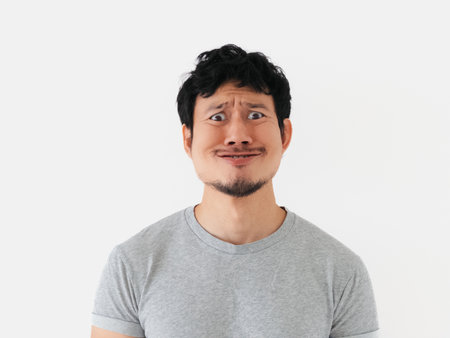 Middle-aged Thai male in a gray T-shirt looking displeased and confused while frowning, brows...