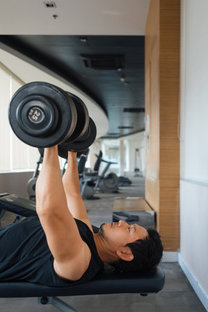 Man working out chest and arm muscles using dumbbells in fitness center