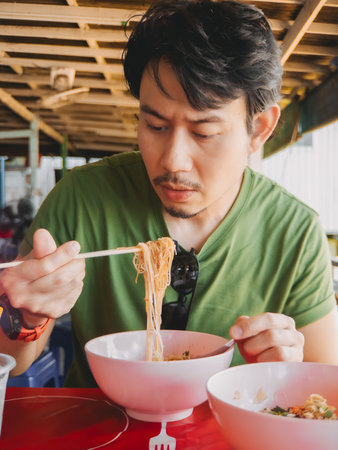 A man truly savoring a bowl of delicious noodles in a vibrant outdoor setting, showcasing the local cuisine beautifullyの写真素材
