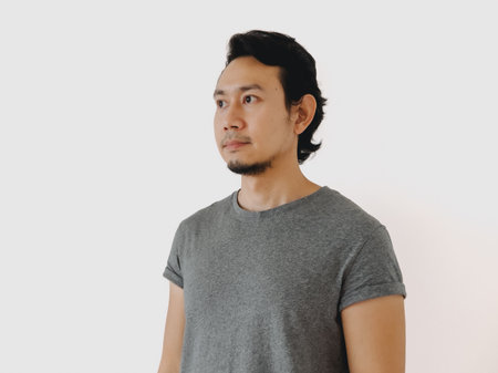 A young man in a stylish gray shirt gazes thoughtfully into the distance, embodying a refined minimalist aestheticの写真素材