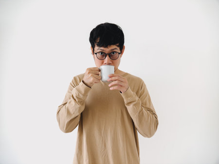Man in a tan shirt is drinking from a white cup. He has glasses on and is looking at the cameraの写真素材