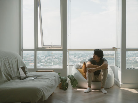 Asian man sitting on the bean bag at the balcony of the condominium, feeling bored and lonely. High quality photoの写真素材