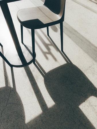Angular shadows of metal chairs fall across a smooth grey floor, creating a dramatic contrast of shapes and lines in natural light.の写真素材