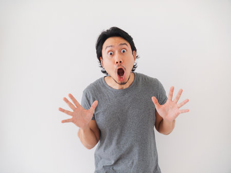 Happy and surprise reaction of Asian man in grey t-shirt isolated on white. High quality photoの写真素材