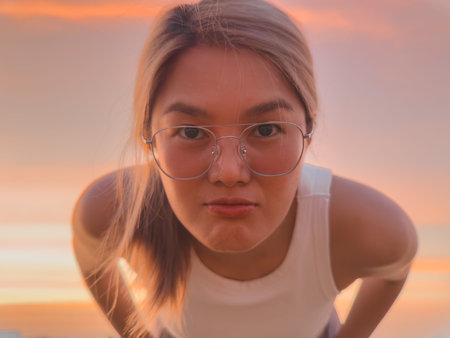 Young woman leaning forward at sunset, closeup portrait with round glasses and inquisitive...
