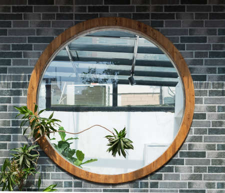 Round window in a brick wall with green plants and a concrete floorの写真素材