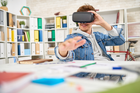 Portrait of young man dressed in casual jeans clothes using virtual reality glasses  in office , taking a break to enjoy 3D game experienceの写真素材