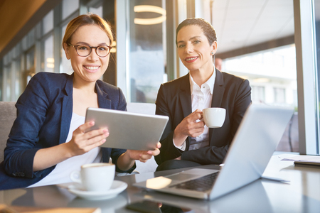 Portrait of two successful businesswomen smiling at camera during work meeting in cafeの写真素材