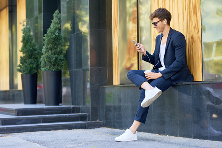 Side view portrait of stylish contemporary man relaxing outdoors enjoying music from  smartphone and smiling happilyの写真素材