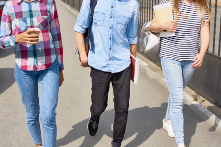 Low section of three high school students walking to class outdoors holding books and coffee cupsの写真素材