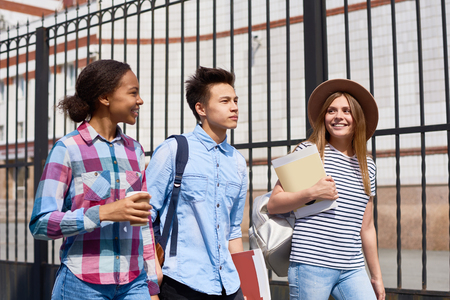 Portrait of three happy high school students walking to class outdoors holding booksの写真素材