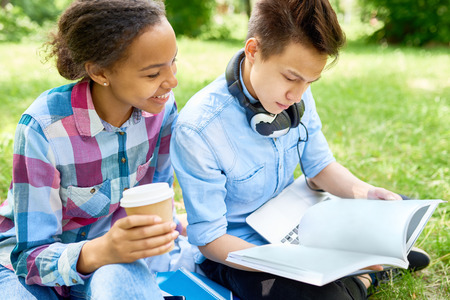 Portrait of two students, boy and girl, studying together sitting on green lawn with books and coffee cupの写真素材