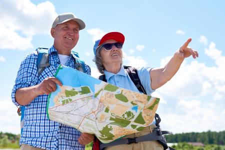 Portrait of active senior couple travelling on hiking trip, pointing to the distance holding guide mapの写真素材