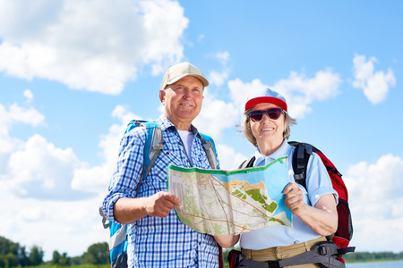 Portrait of active senior couple travelling on hiking trip, smiling looking at camera holding map togetherの写真素材