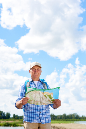 Portrait of active senior man travelling on hiking trip wearing backpack, looking away holding mapの写真素材
