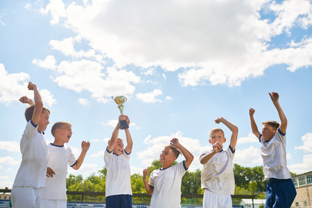 Portrait of boys in junior football team cheering happily and jumping holding trophy cup after winning matchの写真素材