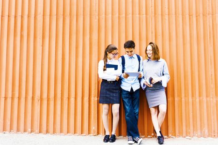 Portrait of three school children standing against bright orange wall using digital tabletの写真素材