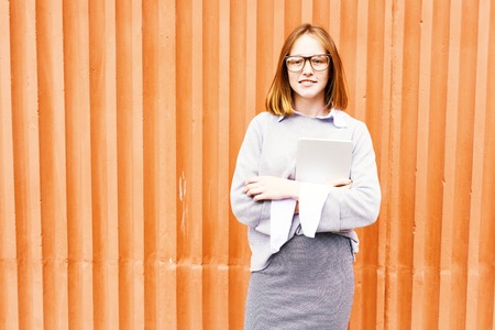 Portrait of smiling teenage school girl with red hair and freckles standing against orange wallの写真素材