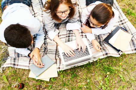 Top view of three school children doing homework during picnic on green lawnの写真素材