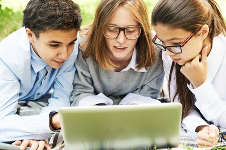 Group of school children using laptop together  outdoors on green lawn, looking at computer screenの写真素材