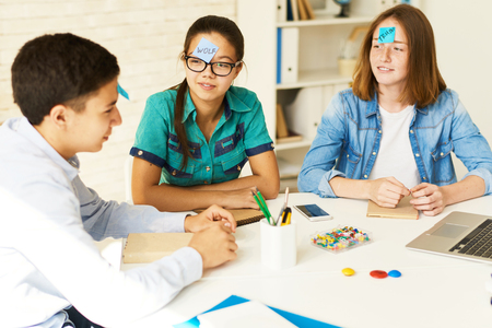 Group of teenagers playing guessing game at table in classroom with names on stickie notesの写真素材