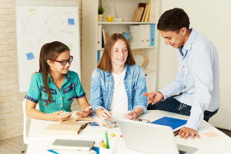 Portrait of three school children preparing for seminar together, discussing project at table in classの写真素材