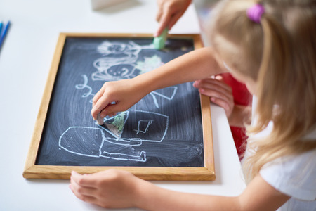 Close-up shot of unrecognizable children sitting at desk and drawing on chalkboard with interestの写真素材