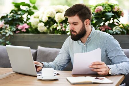 Portrait of young bearded businessman working in comfortable cafe lounge outdoors during coffee breakの写真素材