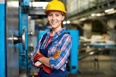 Portrait of beautiful young woman in hardhat smiling confidently at camera enjoying work in modern factoryの写真素材