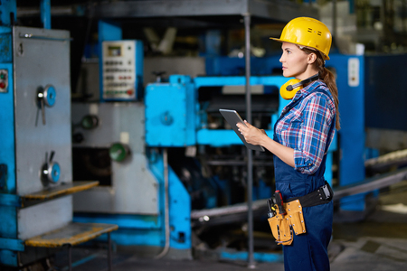 Side view portrait of female machine operator using digital tablet while working with power units in modern factoryの写真素材