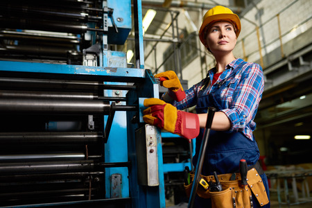 Portrait of female factory worker setting up machine units looking away confidently in modern plantの写真素材