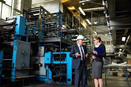 Portrait of senior businessman wearing hardhat talking to assistant manager in modern factory workshopの写真素材
