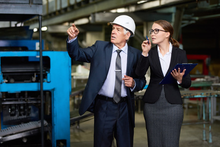 Portrait of young woman giving a tour of modern factory to senior investor or executive manager wearing hardhatの写真素材