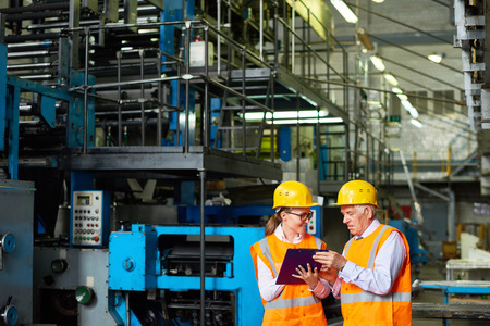Portrait o senior factory worker discussing something with young woman in  modern workshop,  both...