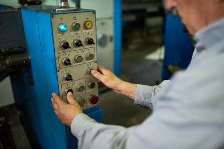 Closeup of unrecognizable senior man operating machines in factory, hands pressing buttons on control panelの写真素材