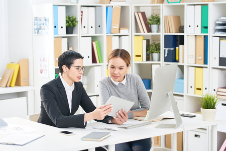 Multi-ethnic group of talented interior designers gathered together at office desk and discussing joint project, they using digital tabletの写真素材