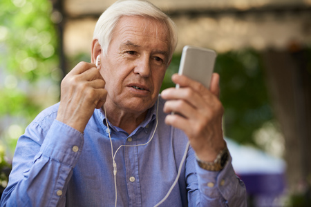 Portrait of senior businessman using video call by smartphone in outdoor cafe loungeの写真素材