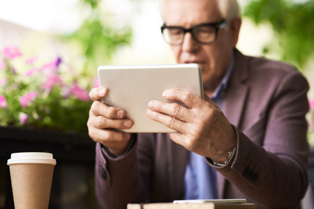 Portrait of senior man using digital tablet in outdoor cafe, focus on male hands holding modern deviceの写真素材