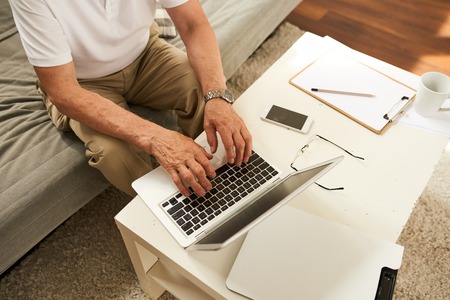 Above view of senior businessman using laptop at home, closeup of male hands typing on keyboard while workingの写真素材
