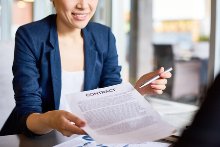 Close-up shot of smiling young white collar worker passing contract and pen to business partner during productive negotiationsの写真素材