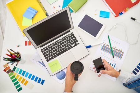 Above view of creative workplace of designer or freelance worker using laptop and smartphone on table with scattered supplies and color palette swatchesの写真素材
