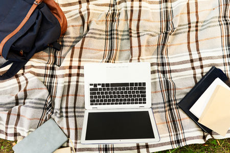 Directly above view of textbooks, modern laptop and school backpack located on checked plaid...