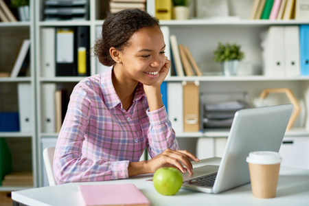 Portrait of smiling African girl studying using laptop in school libraryの写真素材