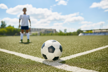 Portrait of unrecognizable teenage boy  in uniform  field ready  to kick the ball on football field, ball in focusの写真素材